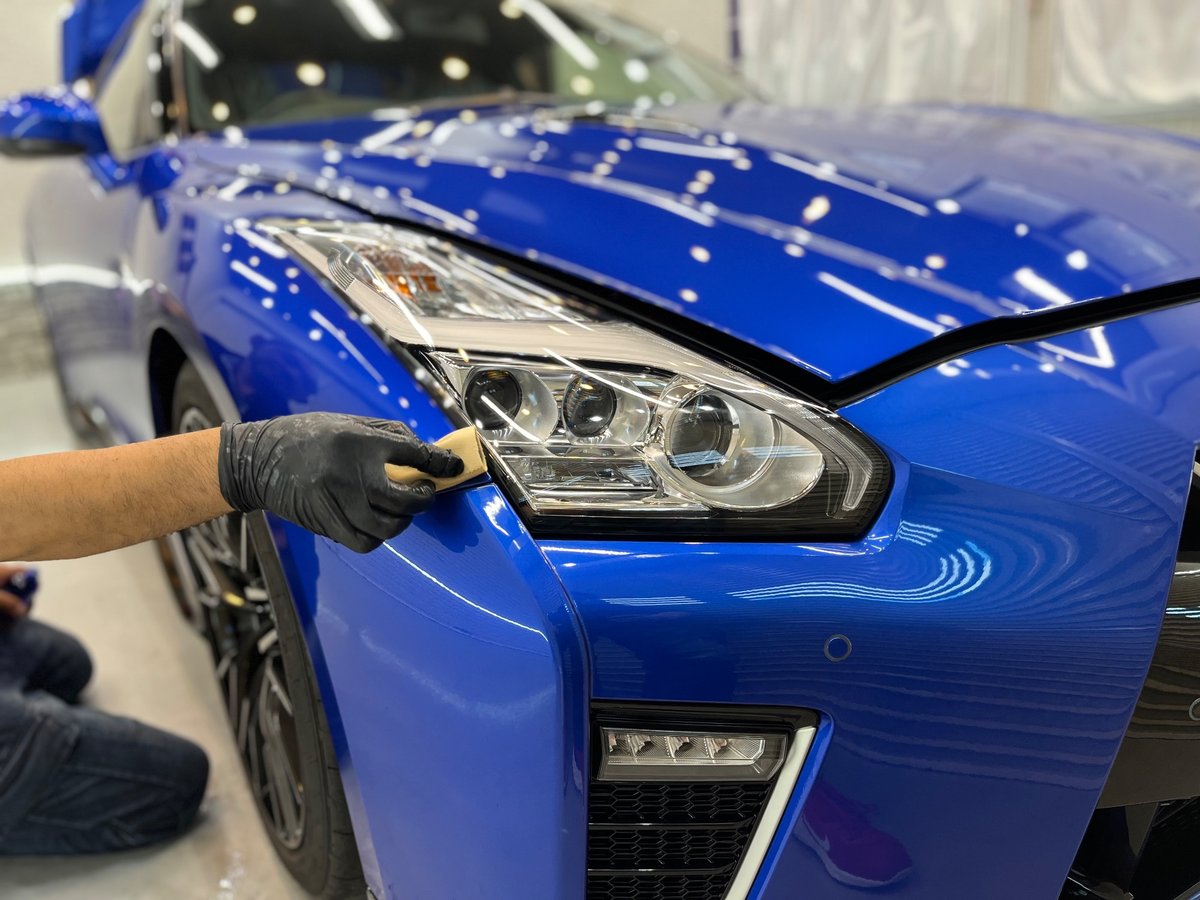 手袋をした手で、GT-R のヘッドライトのまわりにスポンジでコーティングを塗っているところ